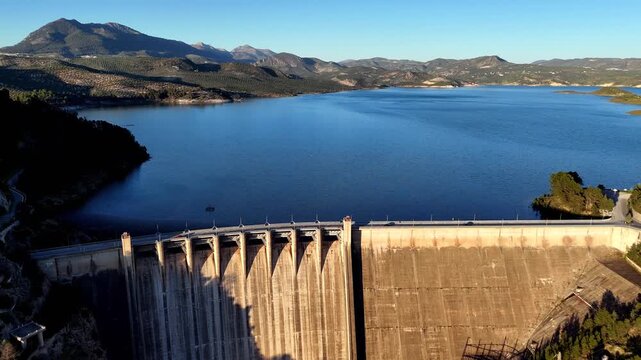 Cinematic drone flyover over Presa de Izn&aacute;jar revealing scenic mountain landscape, reservoir, and dam in Andalusia, Spain, highlighting nature, infrastructure, and travel themes.