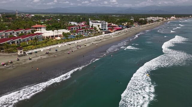 Aerial drone video of Baler Beach in the Philippines captures surfers riding waves and coastline under a bright tropical sun.