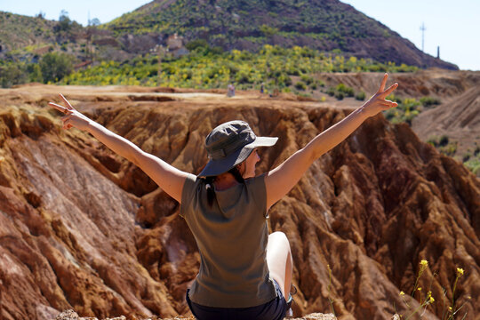 middle-aged woman on a day of trakking with reddish desert landscape of minerals, with textures of eroded rock formations.