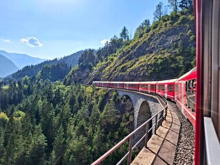 Red train on curved viaduct in the Swiss Alps near St. Moritz, scenic railway journey, Switzerland © Maria