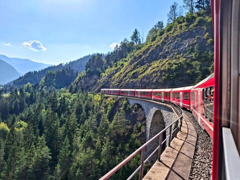 Red train on curved viaduct in the Swiss Alps near St. Moritz, scenic railway journey, Switzerland