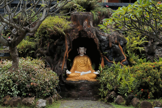 Golden meditating Buddha in rock grotto surrounded by tropical garden