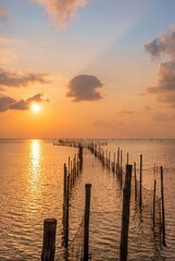 Fototapeta premium Generated AI: Breathtaking Golden Sunset Over Serene Sea with Traditional Wooden Fishing Fences
