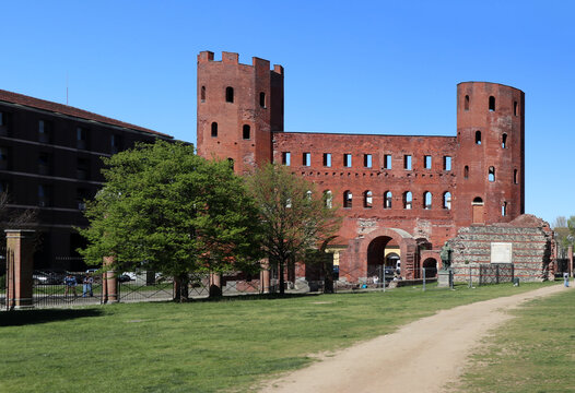 Vista frontale della Porta Palatina a Torino, antica porta romana in mattoni rossi nel parco archeologico con prato verde e cielo azzurro