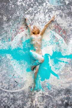 A nude figure stretches gracefully across a canvas flooded with turquoise and white splashes. The pose is powerful yet serene, merging body, gesture, and color in a dynamic abstract flow