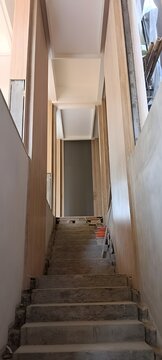 ow angle view of a narrow interior staircase in a house under construction, with raw concrete steps and unfinished wood paneling on the walls. Modern home renovation in progress.