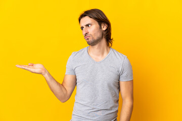 Fototapeta premium Young handsome man isolated on yellow background holding copyspace with doubts