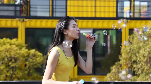 Happy smiling attractive young girl playing outside blowing soap bubbles in the park, smiling, laughing and happy in summer outdoors