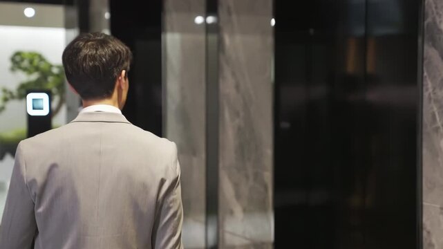 Busy professional businessman in a suit with a briefcase waiting to enter elevator in modern office building during working day, male hand pressing elevator button and looking watch