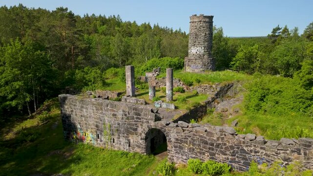 Drone descending over ancient stone walls and arched gateway of Tureborg Castle ruins surrounded by green forest in Uddevalla Sweden