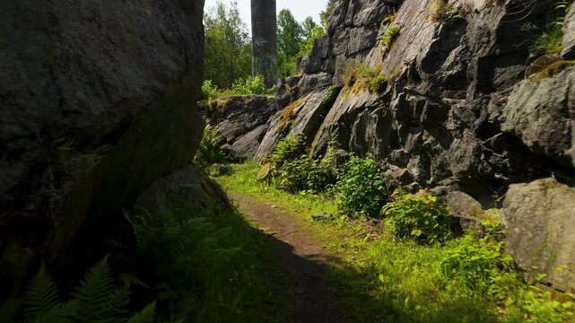 Low altitude aerial drone flight moving along narrow overgrown walkway towards historic Tureborg Castle ruins in Uddevalla Sweden on sunny day