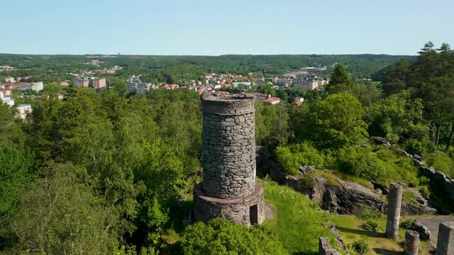 Drone parallax orbits above Tureborg Slott medieval castle ruins on forested hilltop overlooking Gothenburg city, revealing cylindrical stone tower and scattered ancient walls in summer
