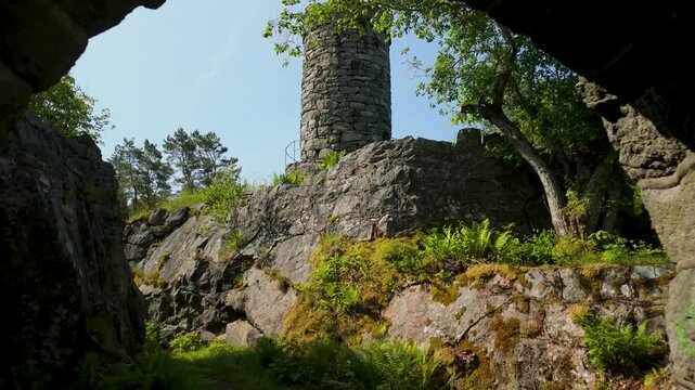 Aerial flying through mossy stone arch revealing medieval round tower of Tureborg Slott perched on granite rocks in Uddevalla, Sweden