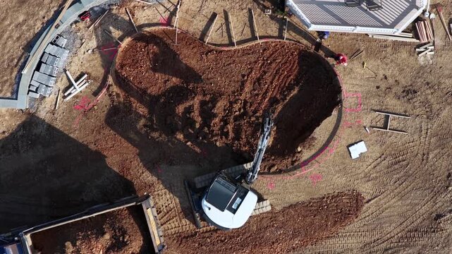 Luxury pool excavation in US backyard, with excavator digging soil, construction layout markings and active landscaping work in sunny suburban residential setting. Aerial top down shot.