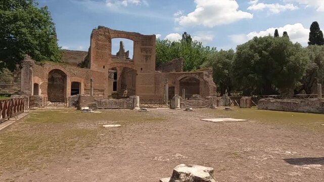 Sunlit ancient Roman ruins at Villa Adriana near Rome, Italy. Crumbling brick arches and stone columns of Hadrian's Villa stand under a bright summer sky.