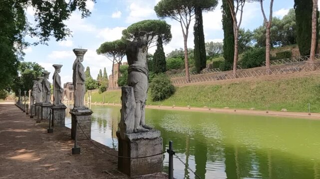 Row of classical caryatid statues lining the Canopus reflecting pool at Hadrian's Villa, Tivoli near Rome. Ancient Roman archaeological site with lush greenery.