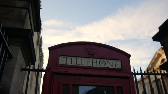 A classic red British telephone box stands against a cloudy sky beside historic stone buildings, perfect for travel, vintage, or urban lifestyle content in London