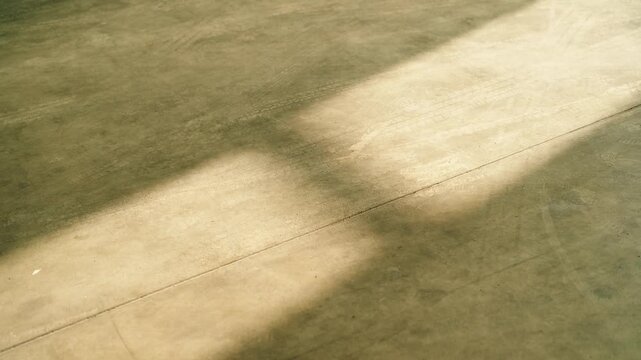 Light and shadow patterns on a workshop floor with visible tire tracks inside an industrial garage.