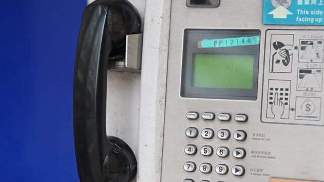 Detailed view of a working public telephone booth with a receiver and keypad. Visual representation of active legacy technology and the survival of traditional telecommunications in a high-tech city.