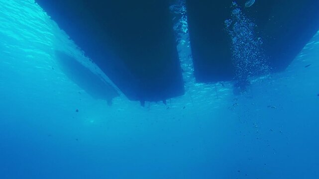 Underwater looking up footage of dark silhouettes of boat hulls and keels cutting through clear blue water. Maritime travel, underwater observation, scuba diving in Red sea in Egypt
