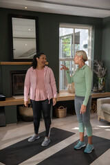 Naklejka premium Senior female friends chatting on black yoga mats in living room beside fireplace wearing sneakers