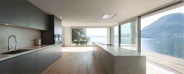 Fototapeta premium Modern kitchen with sleek, dark grey cabinetry, a long island, and large sliding doors that open onto a lake with mountain views