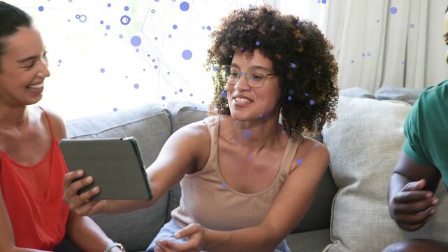 Woman rotating tablet on sofa, friends leaning laughing, camera widening for social sharing