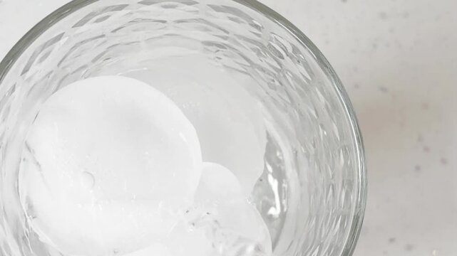 Crystal-clear ice cubes immersed in sparkling water create a refreshing frozen texture with frosty drops and abstract patterns on a clean glass surface. 
