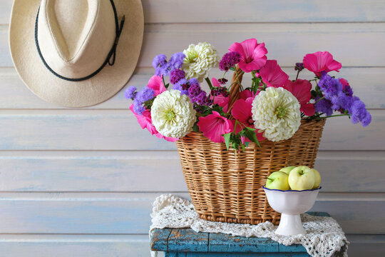 summer cottage still life with garden flowers in a basket and a wide-brimmed hat. bouquet of zinnias, ageratum and lavater. early ripe apples.