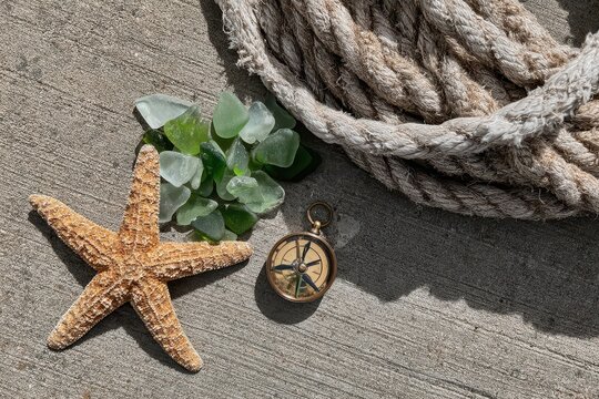 Nautical still life with starfish, sea glass, compass, and rope on a textured concrete surface.