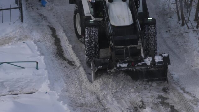 Tractor loader clearing snow from the road in a residential courtyard. Municipal machinery removing snow piles after a heavy blizzard