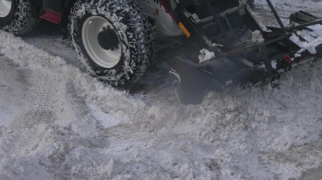 Snow removal tractor scraping large snowdrifts with a bucket on a city road. Process of mechanized clearing of the roadway after heavy snowfall.