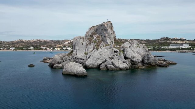 Aerial drone footage of Agios Stefanos Beach and Kastri Island in Kos, Greece. Clear turquoise water, sandy shoreline, and the small chapel on the island captured from above.