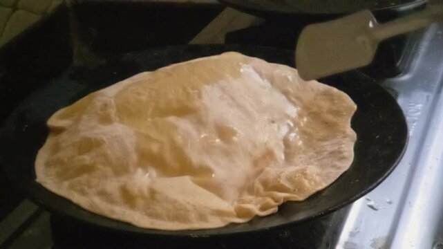 Slow-motion captures oil being brushed onto a Puran Poli. It sizzles on the hot tawa, causing the dough to puff into golden, airy bubbles, creating a perfectly soft, flaky, and delicious texture.