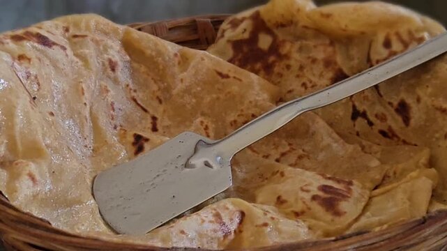 Freshly roasted Puran Poli sits in a rustic bamboo basket, steam escaping through its delicate golden bubbles. The warm, sweet flatbread glows with a buttery sheen after coming off the hot tawa grill.
