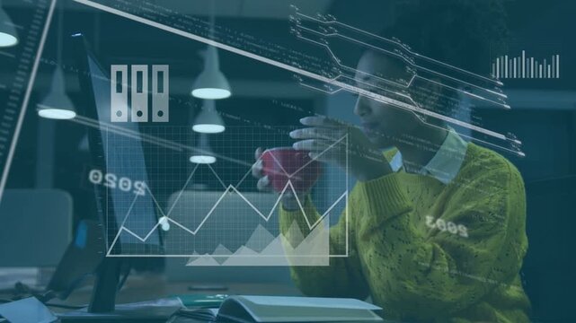 Sipping mug, analyst in yellow top at desk viewing screen, annotating notebook as graphs appearing