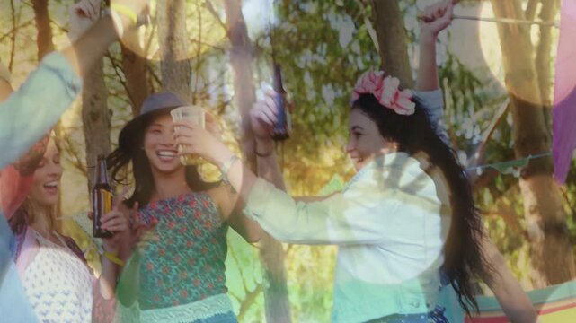 Diverse friends dancing and clinking bottles and plastic cups at campsite, wearing flower crowns