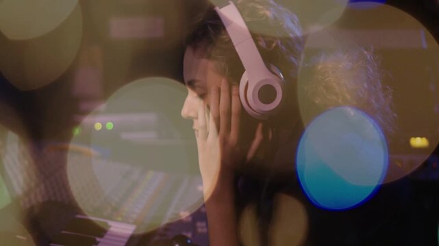 Music producer adjusting headphones, initiating playback and monitoring console with bokeh lights