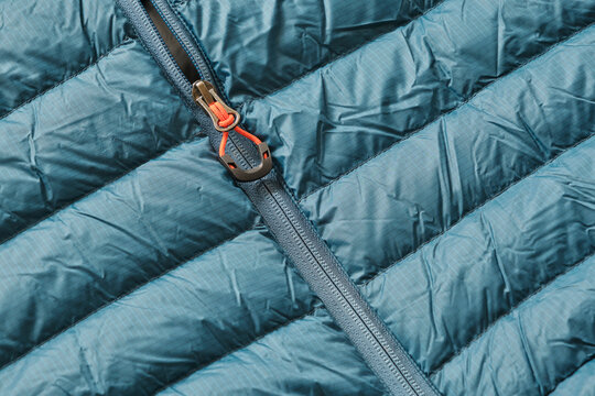 Closeup of a blue down puffer winter jacket with orange details and zipper	