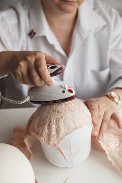 A close-up photo of a seamstress ironing a beige lace bra. Film grain added to the photo.