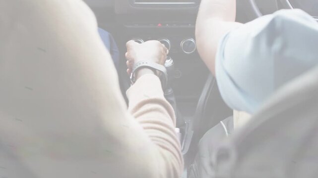 Mature adult reaching gear knob, guiding teen for driving, rotating knob while driver tweaking dial