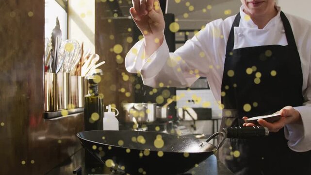 Chef repeating pinches seasoning dish in kitchen over wok, animated yellow orbs obscuring, slowing