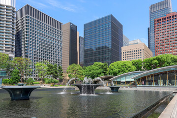 初夏の東京のオフィス街にある都市公園の風景、青空の下に広がる緑豊かな樹木と近代的な高層ビル群　 © 茂明 北村