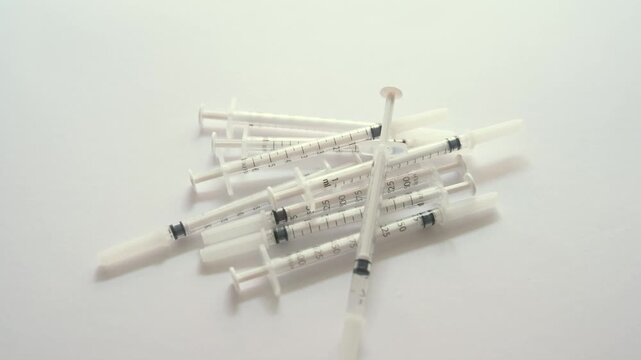 Single new syringe falling in slow motion onto a pile of syringes isolated on a white background