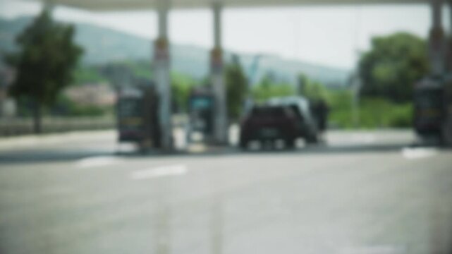 Slow motion medium shot: gas station with intentional blur effect. Distant view of fuel pumps and vehicles at roadside. Soft focus travel and transportation scene.