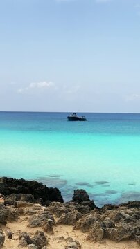 Playa de Migjorn, Formentera, Spain, vertical pan over crystalline turquoise water with luxury yatchs and rugged volcanic rocks on a summer's day