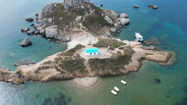 Aerial drone footage of Agios Stefanos Beach and Kastri Island in Kos, Greece. Clear turquoise water, sandy shoreline, and the small chapel on the island captured from above.