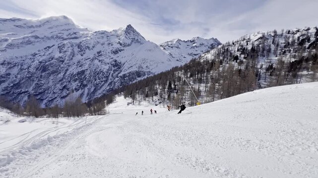 Group of skiers descending a groomed slope in the Alps with majestic snow-capped mountains in the background. Winter sports activity on a sunny day at a ski resort with breathtaking mountain panorama.
