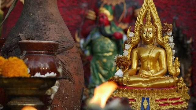 Golden Thai Buddha Statue with Flame Halo Seated on Ornate Base with Candle Flame and Red Offerings