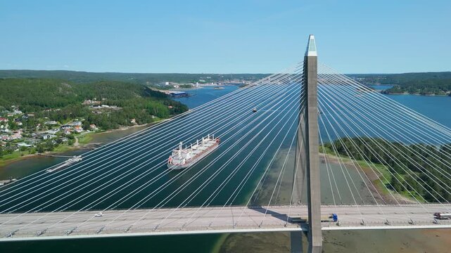 Aerial flyover passing Uddevallabron cable-stayed bridge with bulk carrier cargo ship sailing through Byfjorden fjord in Uddevalla, Sweden